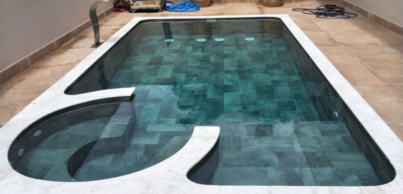 Piscina depois da reforma, com revestimento de manta armada em tom verde-azulado e borda de pedra clara
